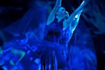Two dancers reaching to the sky with blue light swirling around them