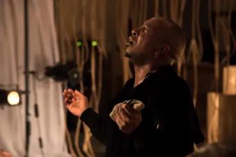 man in a black hoodie with eyes closed in a grimace and hands open upward