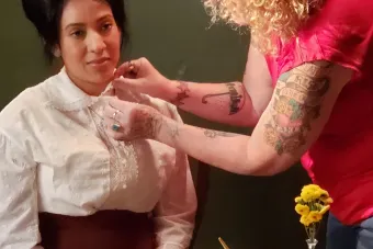 woman with curly blonde hair adjusts the collar of an actress portraying a Texan suffragette
