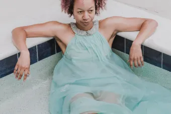 woman with curly brown hair sits in a swimming pool with a long, flowing light blue dress on