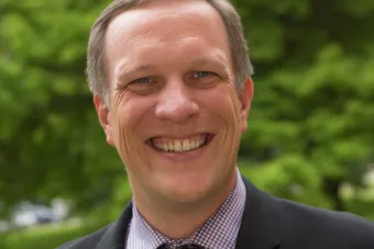 Man in suit standing in front of trees smiling