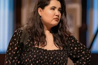 actress with long, wavy, dark-brown hair looking to the side with her left hand on her hip