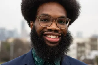 man with dark hair and a beard wearing brown framed glasses and smiling