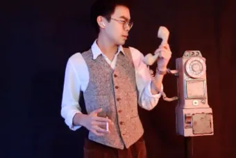 man in a suit vest holding a cigarette and talking on a rotary phone