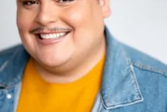 Hispanic individual with short hair and a goatee. They are wearing a yellow shirt and a jean jacket