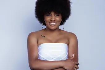 woman with black, curly hair styles in an afro wearing a white dress and large hoop earrings