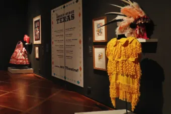 museum exhibit featuring a yellow dress, a feathered hat and a sign reading "The Great Stage of Texas"