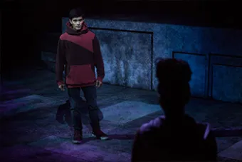 two figures stand on a dimly lit stage