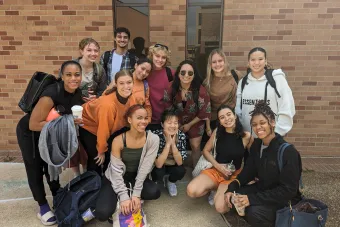 13 UT dance students smile together in front of a brick wall at the ACDA regional conference