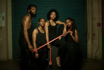 four student artists in black pants and tank tops pose together, holding red tape