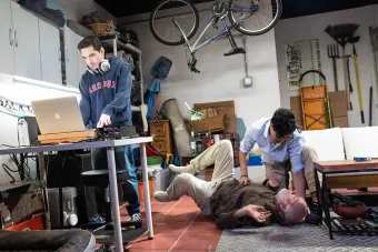 Three actors perform in TOROS, one standing behind a laptop, in what looks like a garage studio space