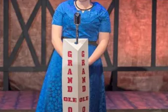 Lilly Lane Stafford stands on a stage at a microphone dressed as Patsy Cline.