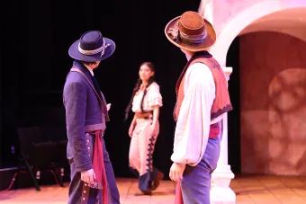 Two performers turn back to look at a third performer, all wearing detailed costumes designed by a graduate student