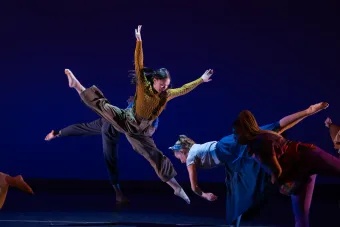 A dancer photographed mid-leap, their arms stretching upward