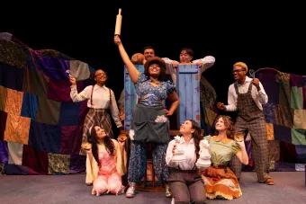 A girl in a blue dress upholds a rolling pin