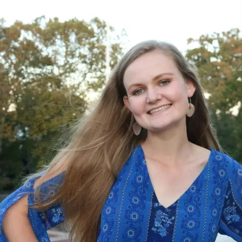 A woman wearing a blue shirt places her hands on her hips and smiles
