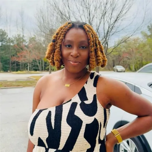 A woman with blonde locs smiles with her hand on her hip