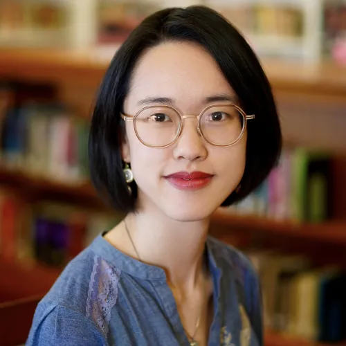 A woman with short black hair and glasses looks forward