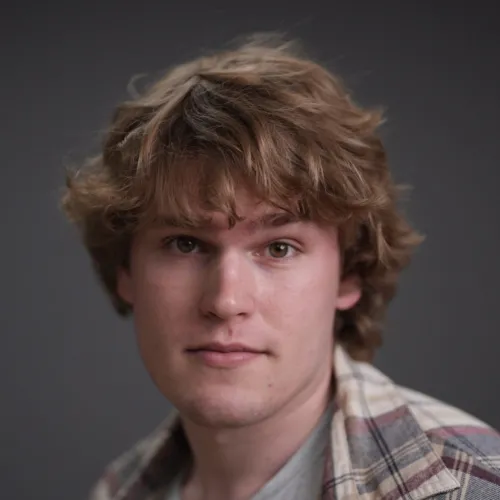 A man with dark blonde hair wearing a flannel looks forward