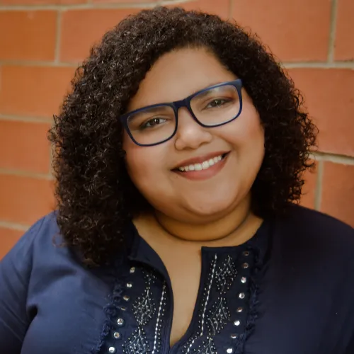 Headshot of a woman with dark curly hair and a dark blue blouse