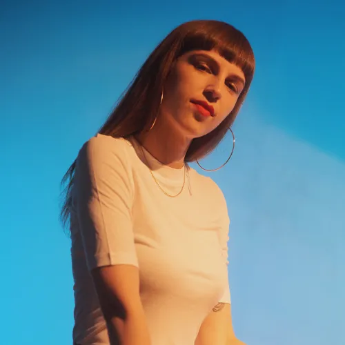 A woman with bangs stand in front of a blue background