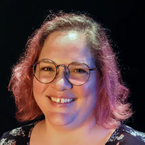 A woman with pink hair and glasses smiles