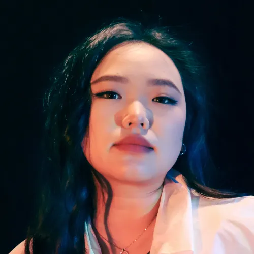 A woman with long black hair looks toward the camera