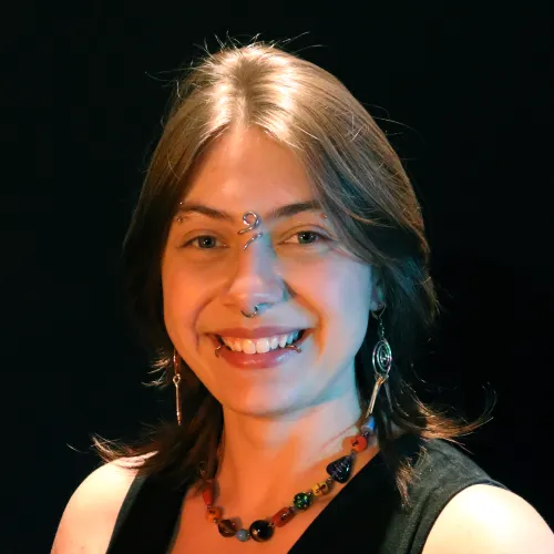 A person with long brown hair and piercings smiles