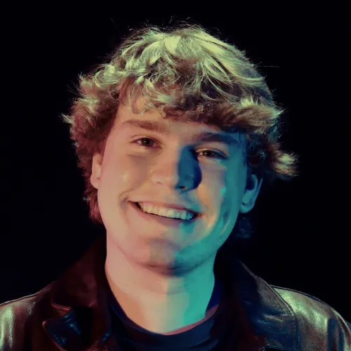 A man with short hair angles his head and smiles