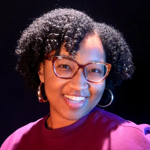 A woman with short curly hair and glasses smiles
