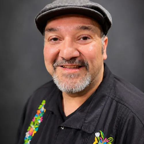 man smiling with a salt and pepper goatee flat grey cap and black guayabera shirt