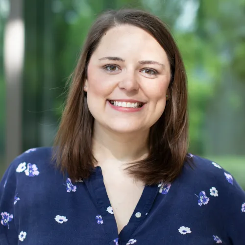A woman with brown hair wearing a blue blouse smiles