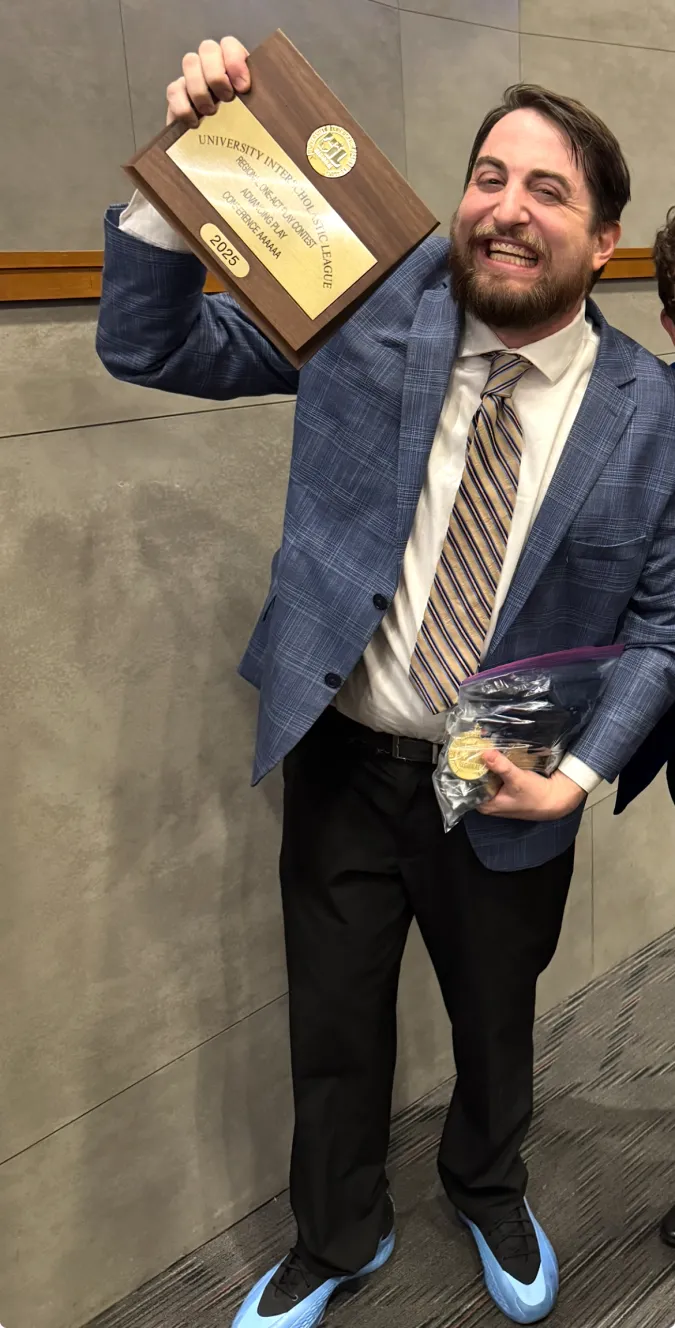 Alum and theatre educator Cody Edgar smiles and holds up an Advancing State One-Act Play plaque