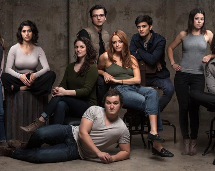 fifteen actors in front of a gray wall