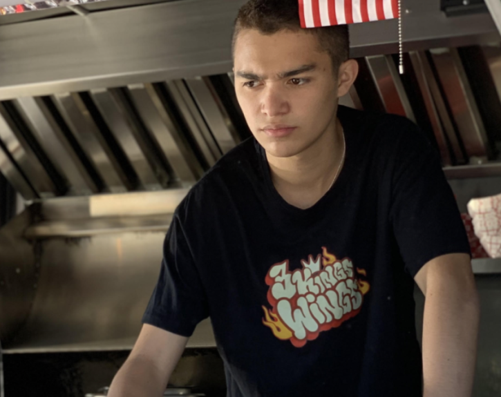 A person wearing a black t shirt looks serious in a kitchen