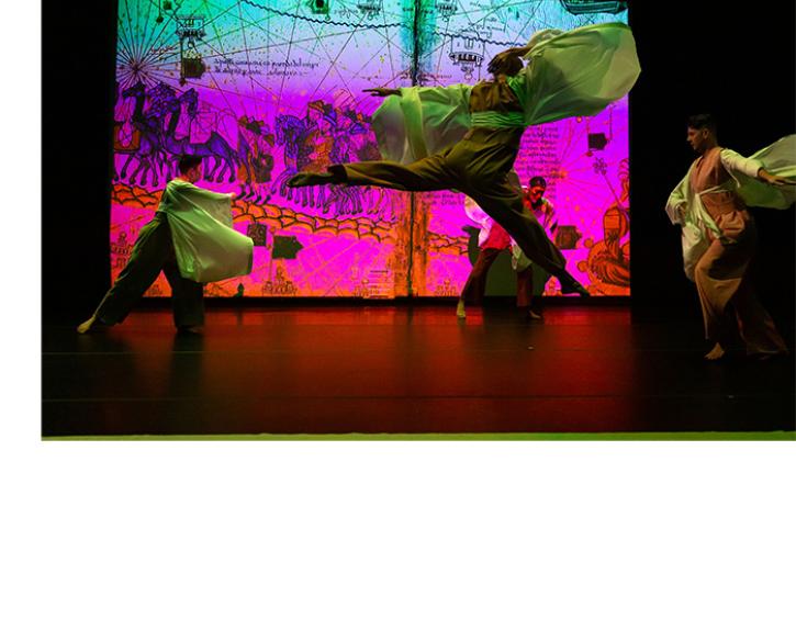 Dancer mid-jump, their sleeves flowing out beside them, with other dancers and an intricate projection of historical art and maps in the background