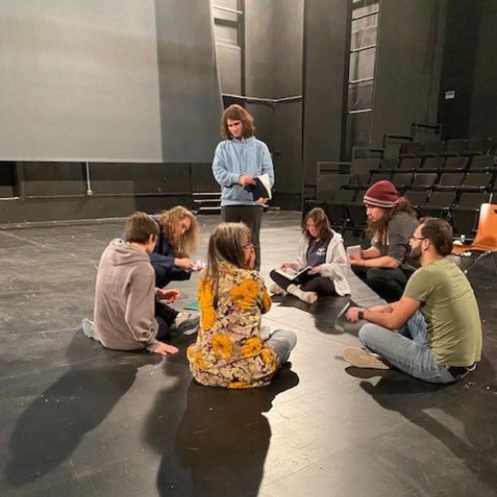 A circle of students sit around a teacher