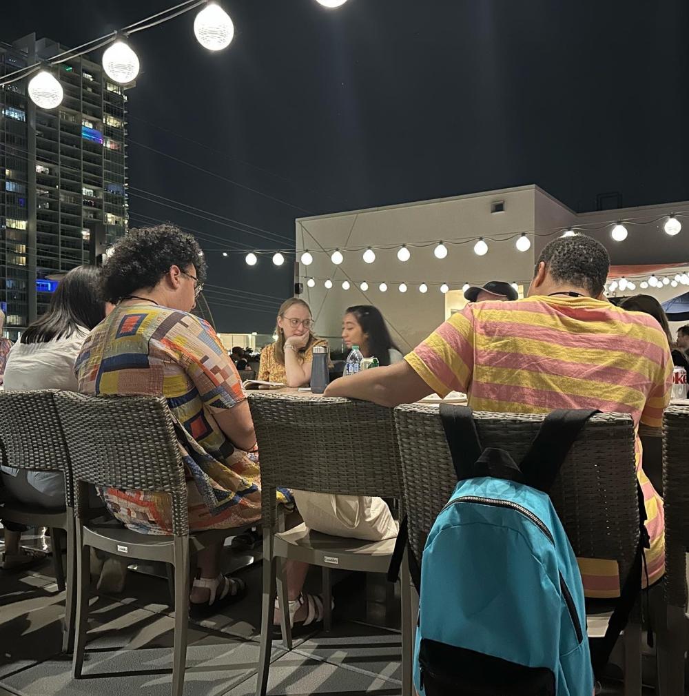 UT alumni, students and other TYA/USA attendees sit around a table for a reading of a play, with string lights shining above their heads