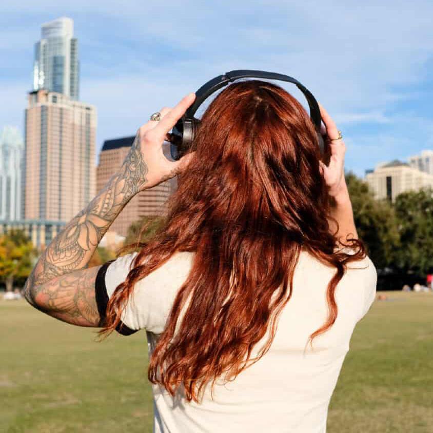 A photo of a person with long red hair putting on headphones, looking at the Austin skyline