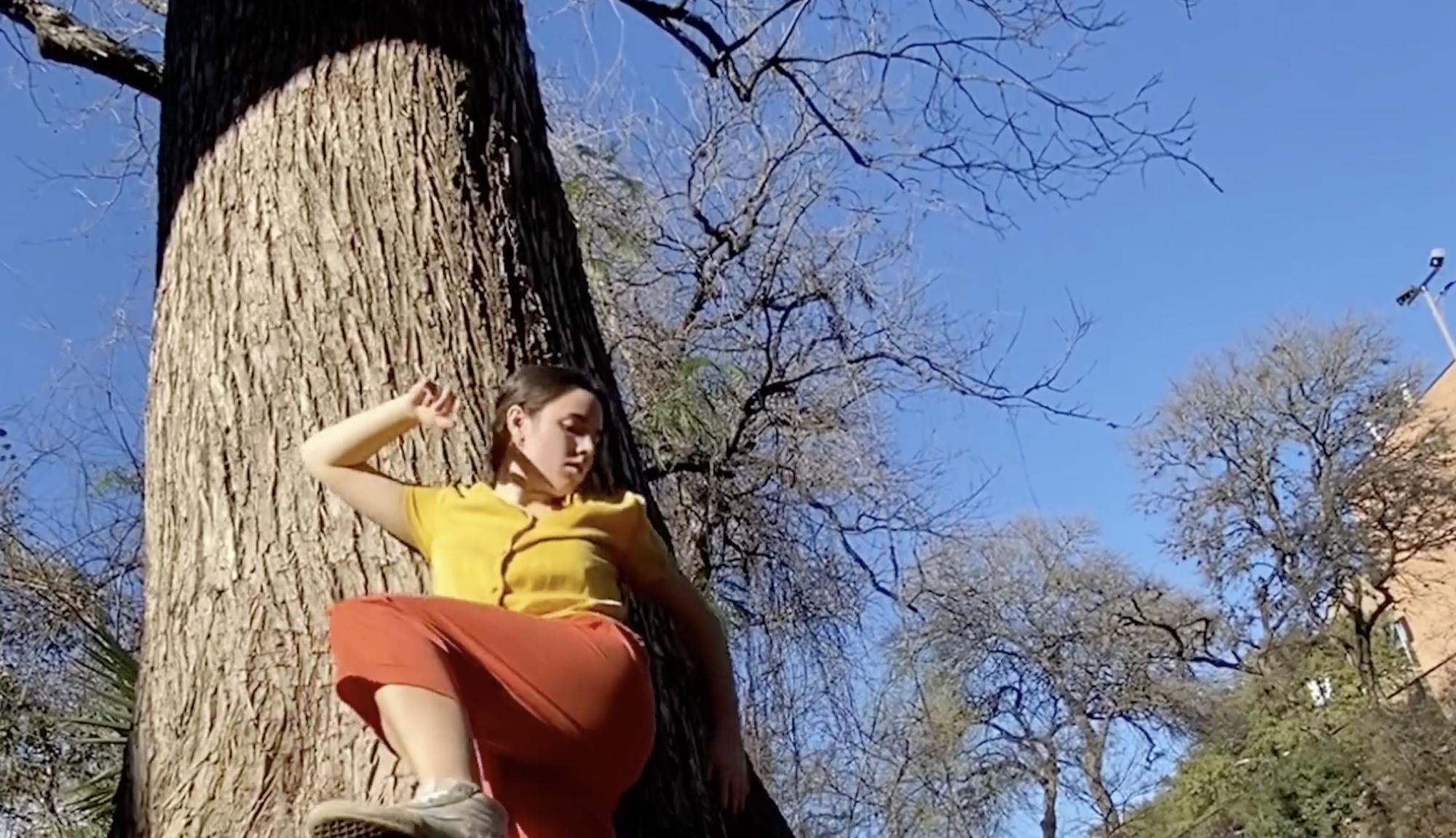 dancer leans against a tree with their left leg and right arm raised