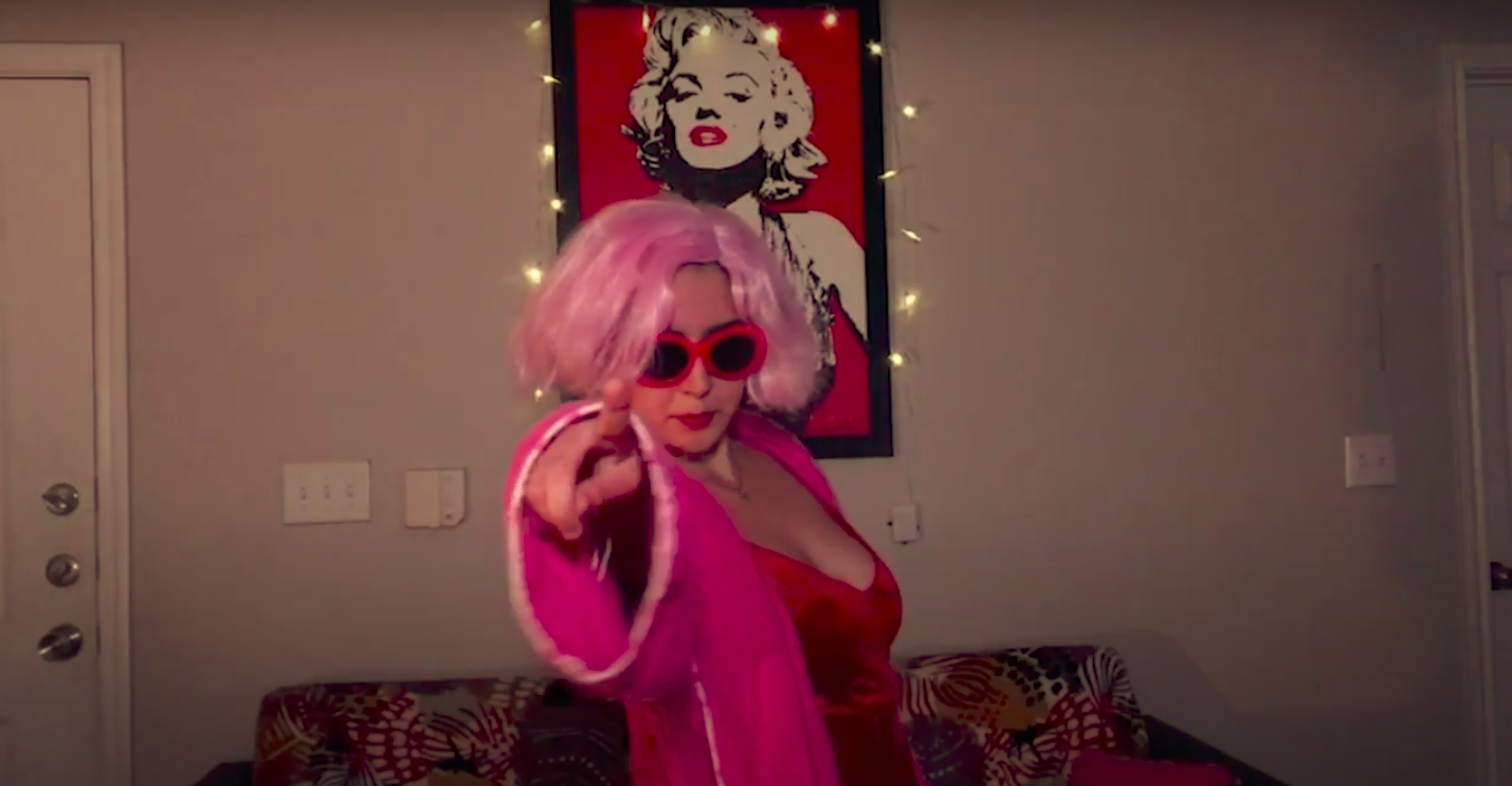 actress wearing a pink wig and sun glasses points with her right hand