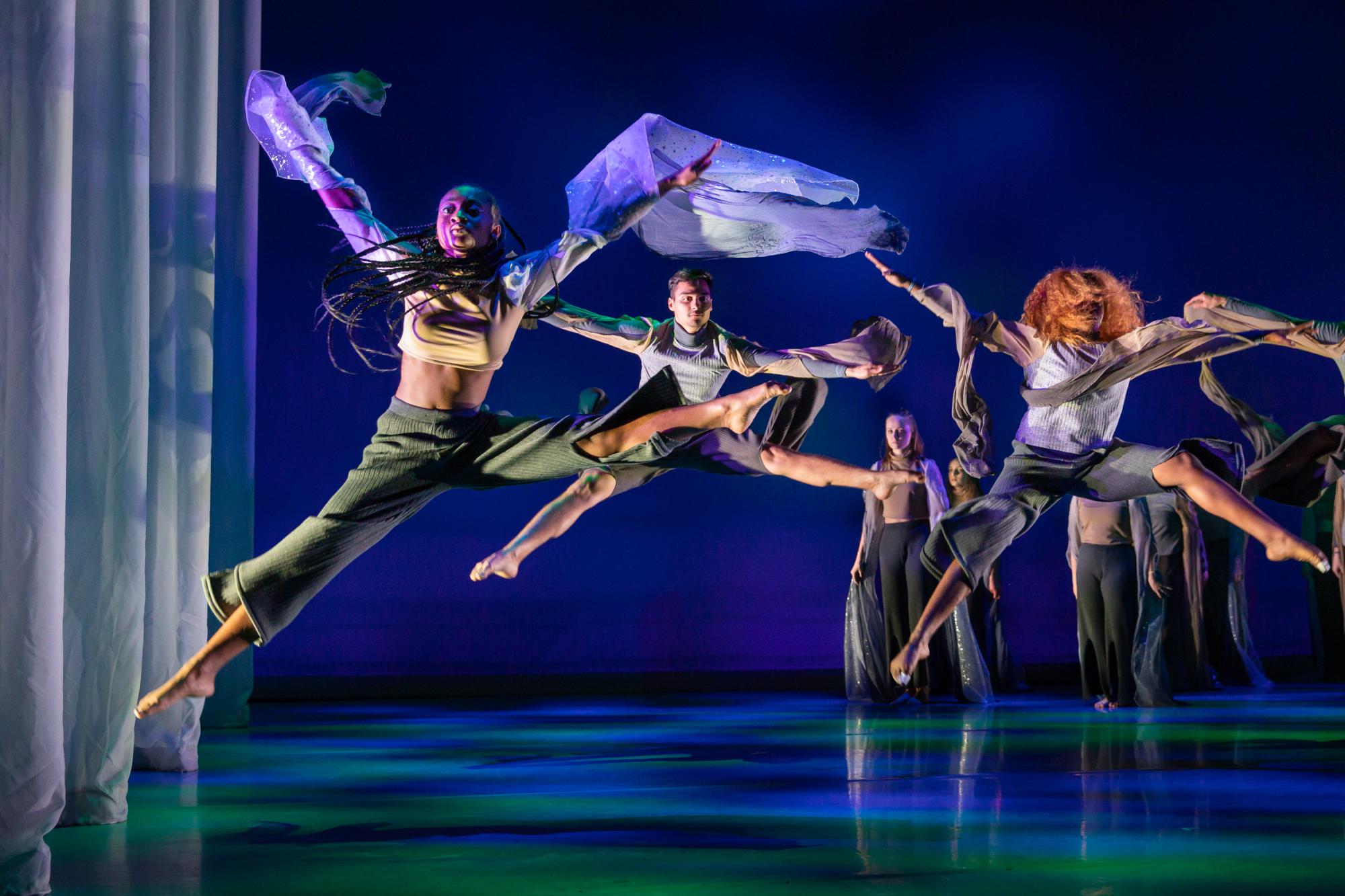 three dancers leap on stage, their arms and legs stretched out in V formations