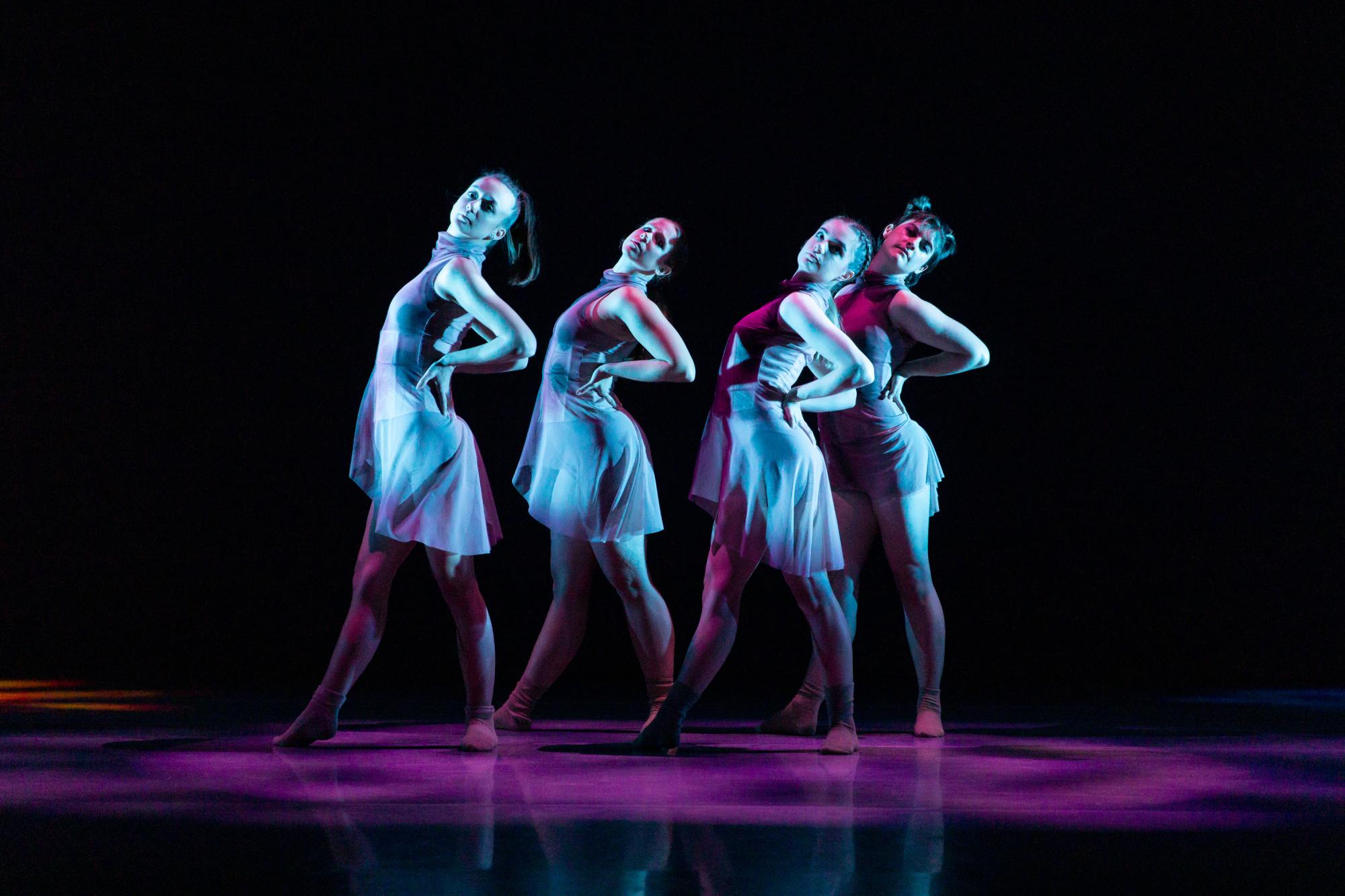 four dancers pose with their hands on their hips, tilting their shoulders backwards