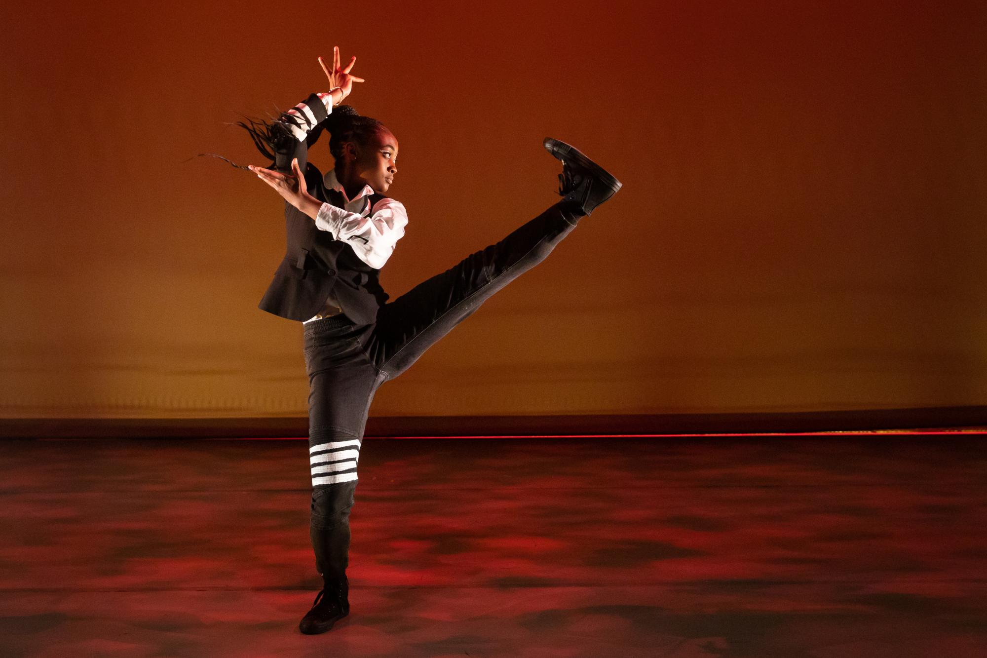 dancer with her braids pulled into a ponytail kicks her leg out in front of her, holding her arms at angles around her head