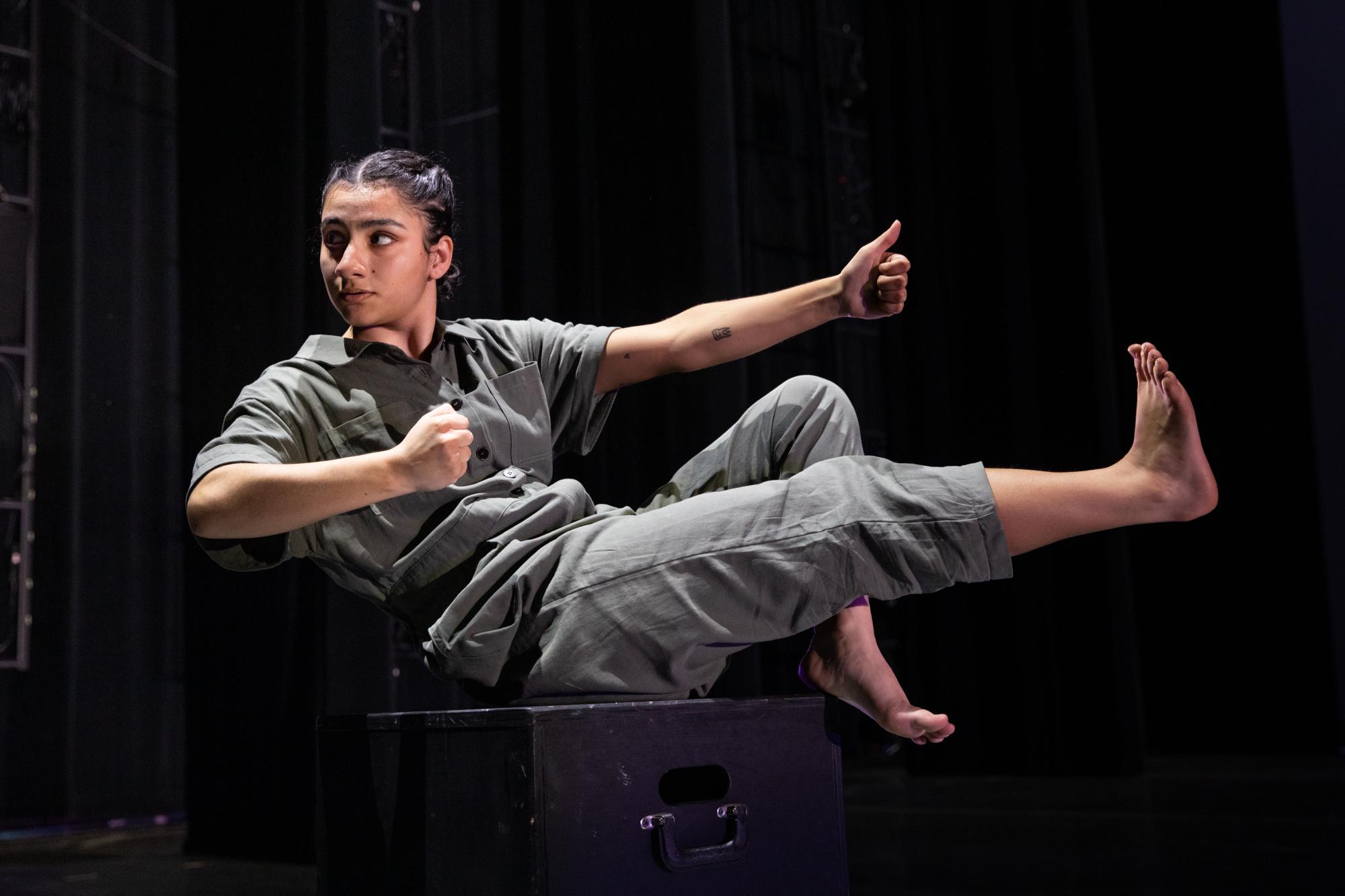 dancer sits on a black block, holding their right leg and left arm out in front of them