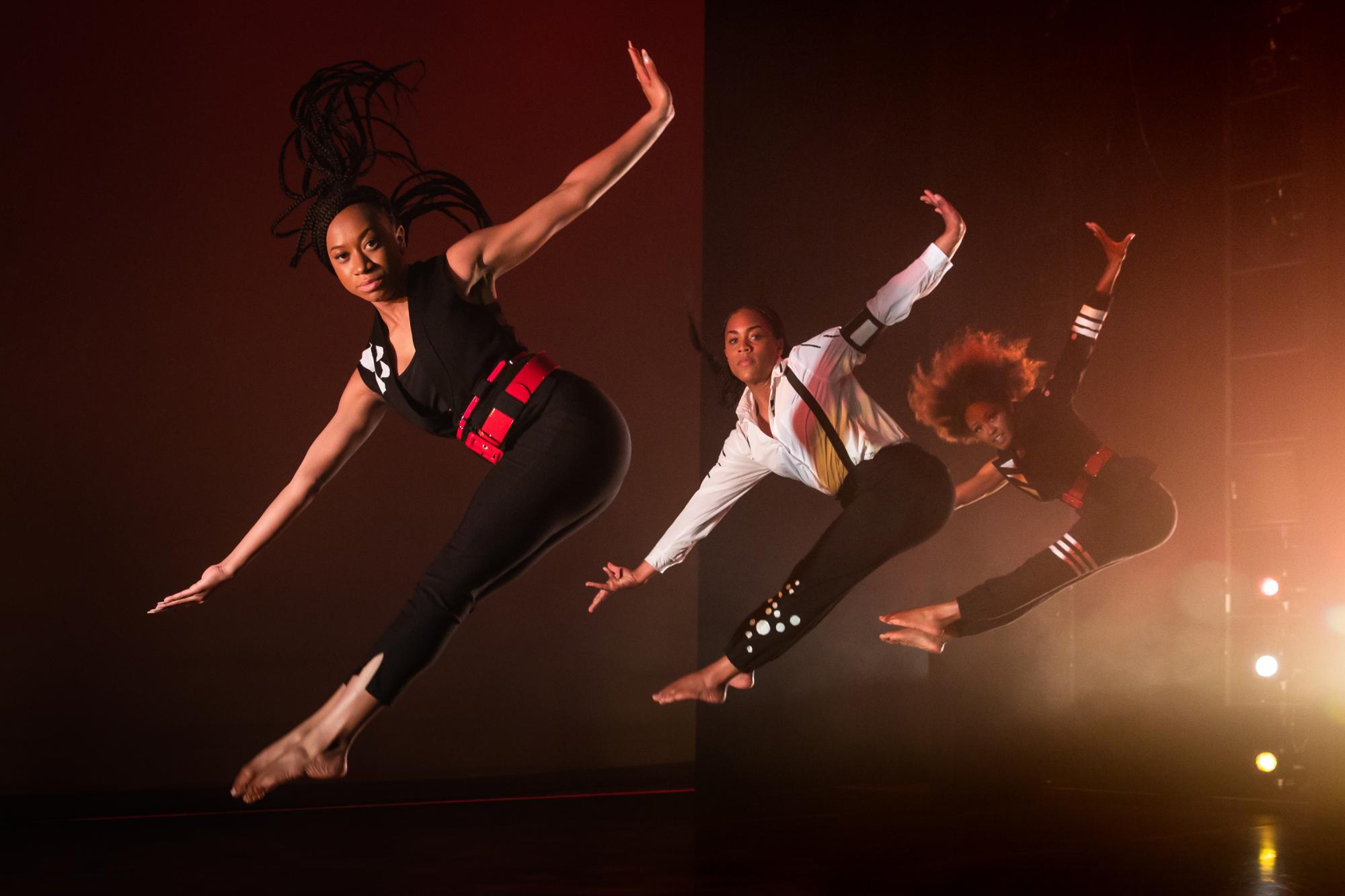 three dancers photographed in mid-jump, their toes pointed and their arms stretched out beside them