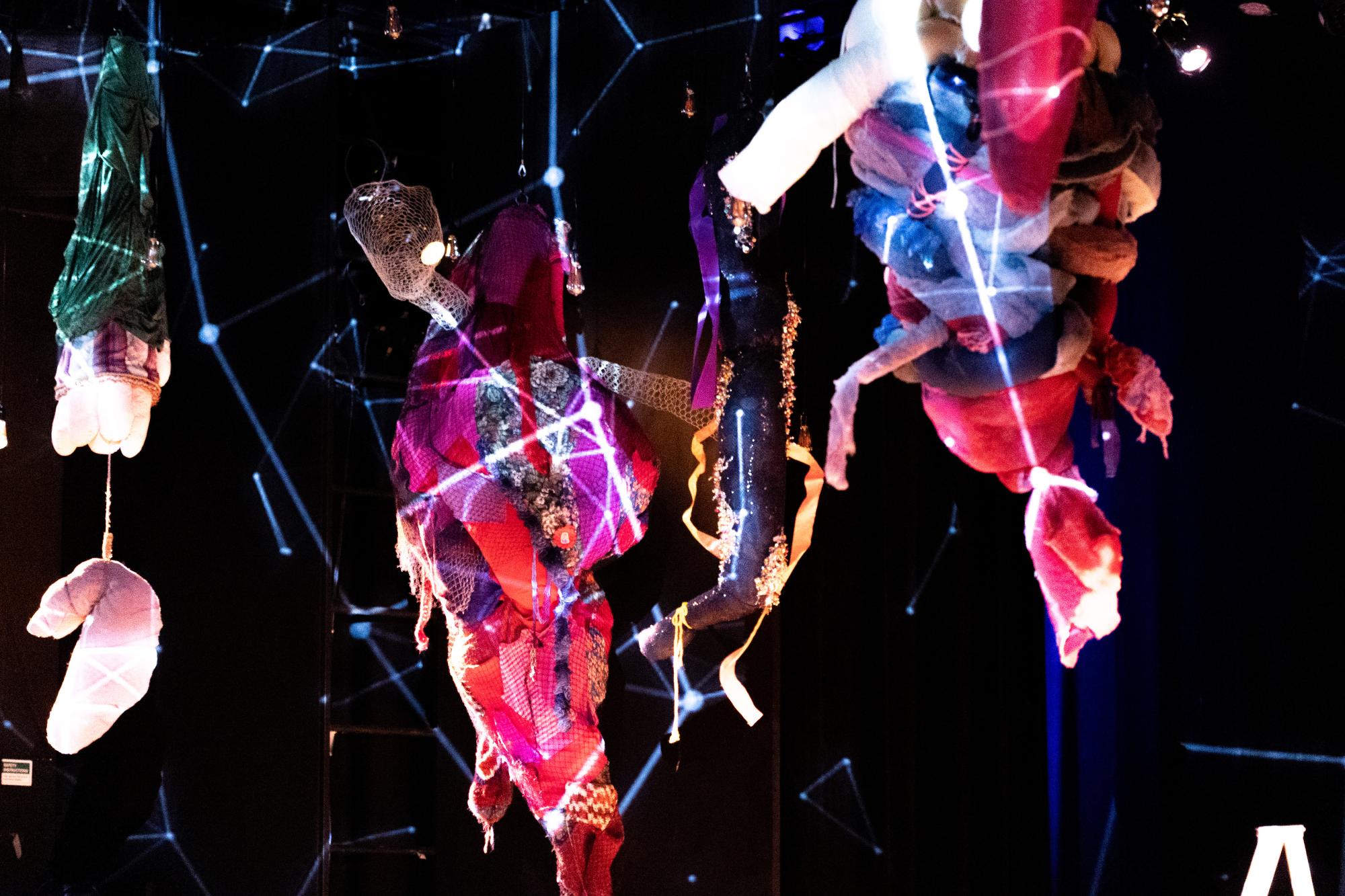 stylized sculptures hang from the ceiling in the Brockett Theatre, with constellations projected on them