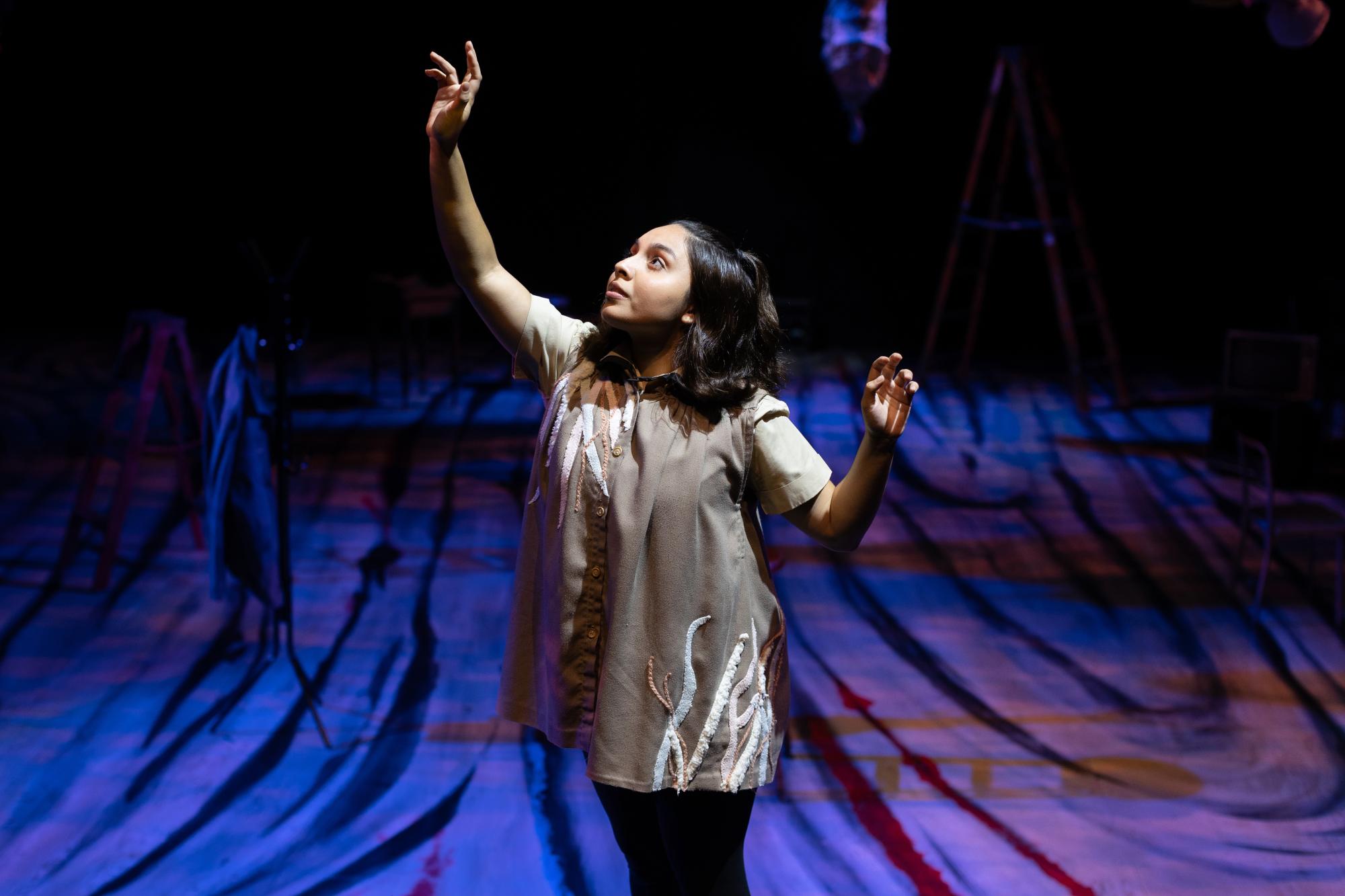 woman with her arms stretched out curiously, washed in blue stage light