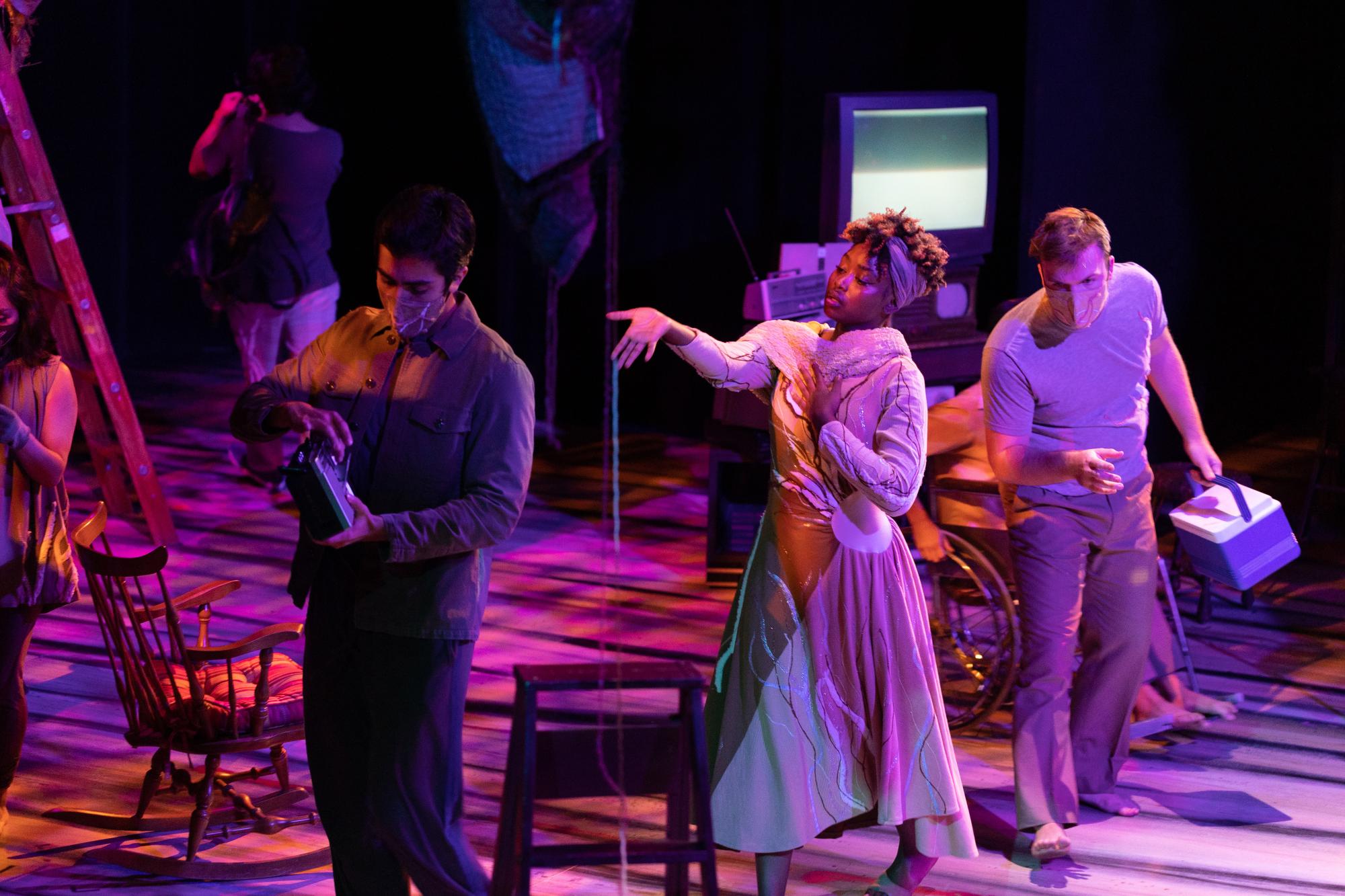 an ensemble of actors walk across the stage without acknowledging one another, interacting with props they are holding