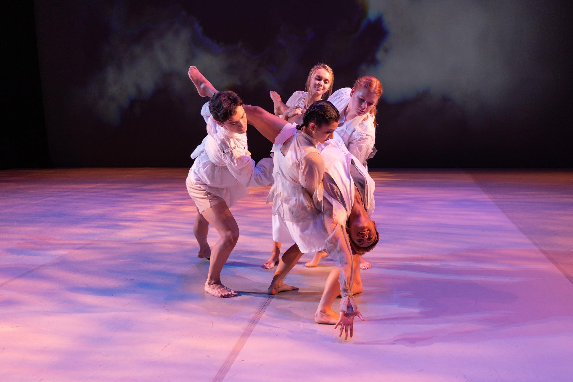 three dancers in all white hold up a fourth dancer, who leans back and stretches her left arm forward